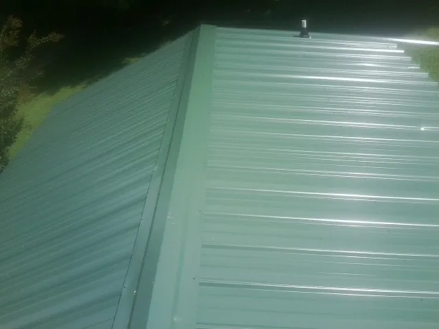 New green metal panels meeting at the ridge of a roof — Flat Roof Repair work by our crew in Peru